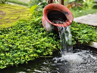 Clay pot decorative fountain pouring water into a garden pond
