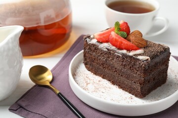 Piece of delicious chocolate cake with strawberry, almonds and tea on table, closeup