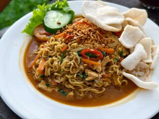 A plate of spicy fried noodles or mie goreng nyemek served with vegetables, shredded chicken, fried...