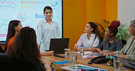 Indian young female old boss lady team leader show chart white board learn study graph data growth work place adult girl talk speak share stock trade idea plan staff group job office day