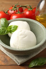 Tasty mozzarella balls, tomatoes and basil on wooden table, closeup