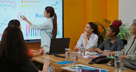 Indian young female old boss lady team leader show chart white board learn study graph data growth work place adult girl talk speak share stock trade idea plan staff group job office day