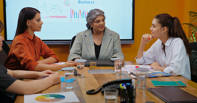 Indian old boss ceo woman lady show stock data chart paper growth talk share new deal ideas plan young adult expert girl staff group intern team speak do work day task make new deal at job place