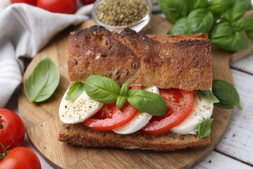 Tasty sandwich with mozzarella cheese, tomatoes and basil on white wooden table, closeup
