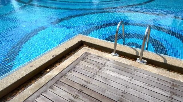 A swimming pool with blue tiles and a wooden deck on a sunny day