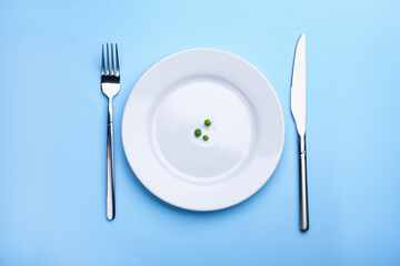 Plate with fresh green peas and cutlery on light blue background, top view