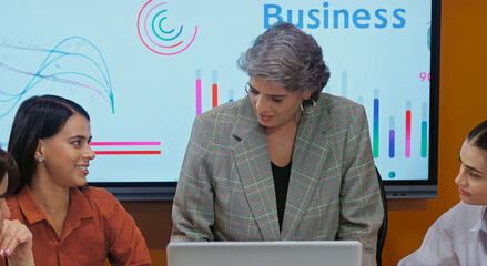 Indian asian young female old senior boss lady team leader show chart board learn study graph data growth work place adult girl talk speak share stock trade idea plan staff group job office day
