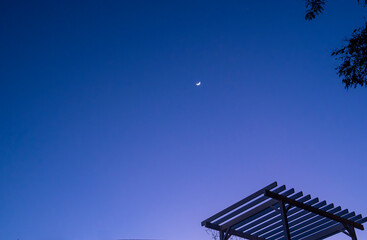 A large moon is visible in the sky above a patio with a gazebo. The sky is dark and the moon is the only light source