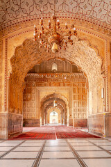 The majestic interior of Badshahi Mosque reveals stunning Mughal arches and intricately patterned ceilings, bathed in soft light, offering a glimpse into historical grandeur and Islamic artistry.