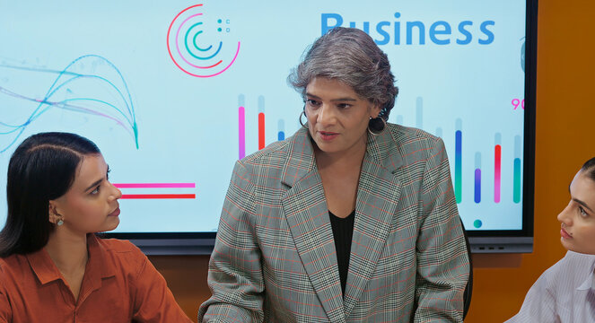 Indian asian young female old senior boss lady team leader show chart board learn study graph data growth work place adult girl talk speak share stock trade idea plan staff group job office day