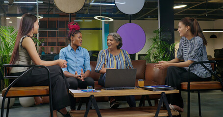 Indian old aged boss lady do work talk good news new share deal speak ideas plan job place happy female girl staff group team sitting on chair sofa couch use laptop look screen at office