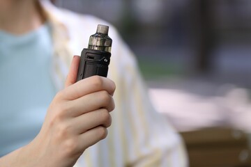 Fototapeta premium Young woman with electronic smoking device outdoors, closeup. Space for text