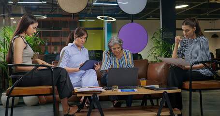 Indian Asian serious busy woman sitting sofa couch chair desk table use laptop look camera typing...