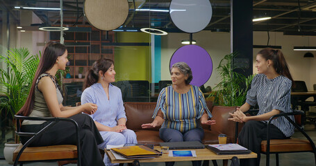 Indian young adult woman talk gossip with old aged boss ceo lady enjoy day spend time job place happy smiling female girl expert staff team leader speak talk share good news do new work deal at office