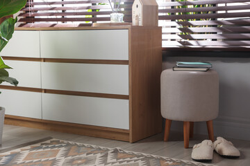 Stylish pouf with books and slippers near chest of drawers at home