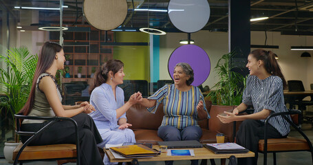 Indian young adult woman talk gossip with old aged boss ceo lady enjoy day spend time job place happy female girl expert staff team speak share good news do new work deal at office