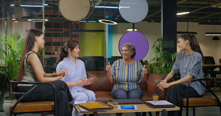 Indian young adult woman talk gossip with old aged boss ceo lady enjoy day spend time job place happy female girl staff team speak do new work deal share good news show thumbs up at office