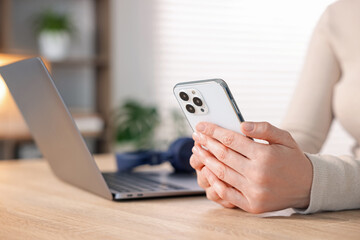 Woman using modern smartphone at wooden table indoors, closeup