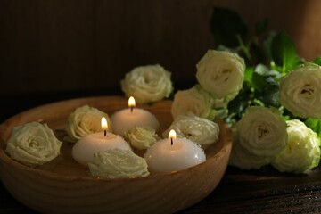 Burning candles, water and rose flowers in bowl on wooden table, closeup
