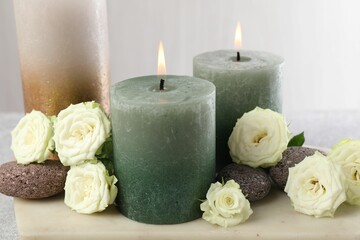 Burning candles, stones and rose flowers on table, closeup
