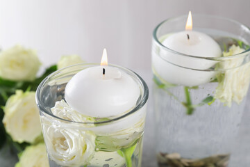 Burning candles in glasses with water and rose flowers on table, closeup