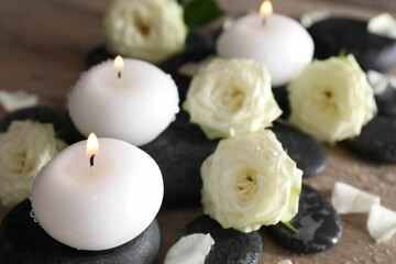 Burning candles, stones and rose flowers on wooden table, closeup