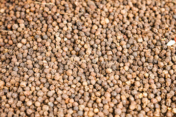 Close-up of whole black peppercorns, showcasing natural variation in color and surface detail. A...