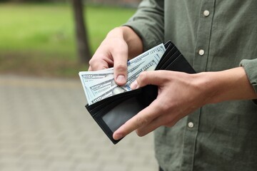 Man putting money into wallet outdoors, closeup