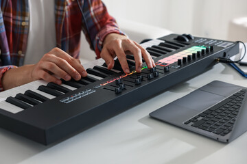 Man working with MIDI keyboard at white table indoors, closeup