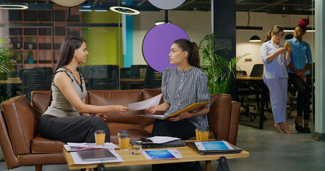 Indian young adult gen z expert girl staff talk with boss lady show chart paper share new task data...