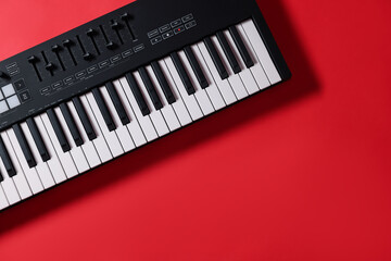 Fototapeta premium One portable MIDI keyboard on red background, top view. Space for text