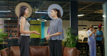 Indian young adult gen z happy expert girl staff talk with boss lady share new task job place two busy female pair standing do work speak casual day plan ideas make new deal time indoor office