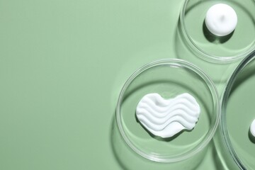Different cosmetic products in Petri dishes on green background, flat lay. Space for text