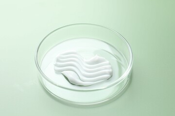 Cosmetic product in Petri dish on green background, closeup