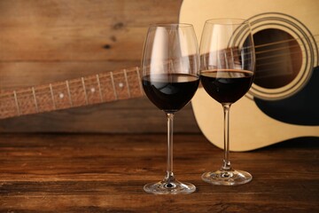 Acoustic guitar and glasses of red wine on wooden table. Space for text