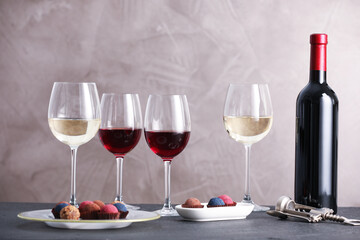Delicious truffle bonbons and wine on black table against grey background
