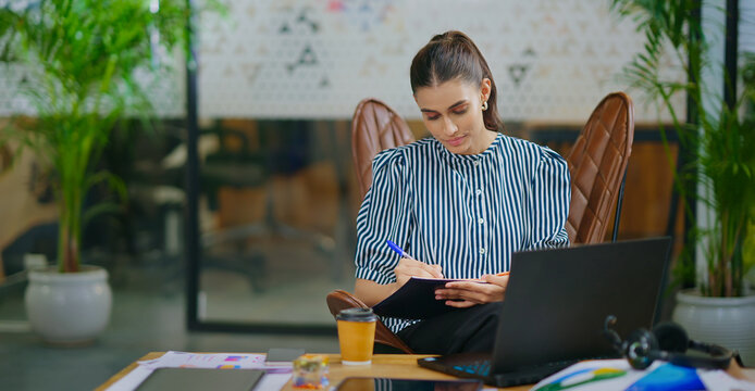 Indian gen z busy woman lady sitting chair use laptop on desk table look screen check email job office place young adult expert girl staff female do online work search day task data new idea plan