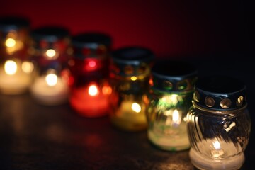 Many grave candles on black table against red background, closeup