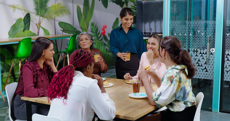 Happy asian woman girl old lady senior group team talk gossip eat sandwich share lunch indoor office work place indian diverse female sitting around table enjoy breakfast tasty juice cup have fun joy