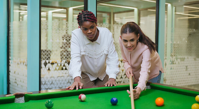 Indian happy young adult gen z woman lady hold cue stick hit ball play sport game on pool table after work girl female staff enjoy good break time spend day have fun joy job place - Powered by Adobe