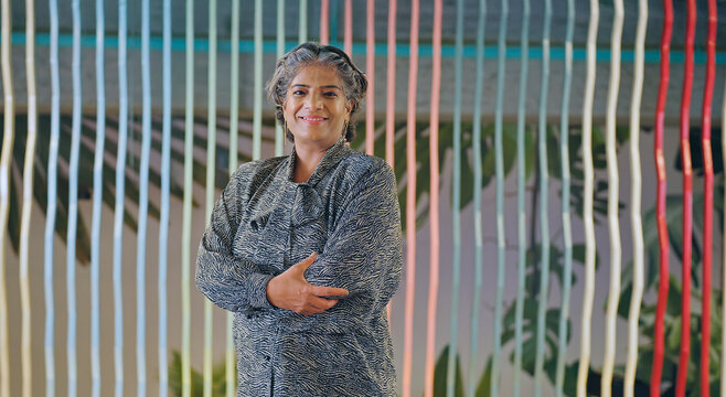 Indian happy old aged gray haired women boss lady leader ceo standing proud cross arms look camera indoor work place Asian alone older elder adult female staff staring cam do pose fold hand job office