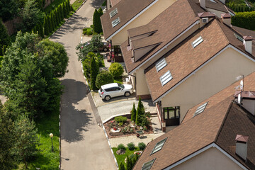 Aerial view of suburban house with brown roof, white car and landscaped garden