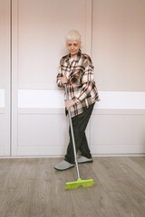 An elderly woman with a short haircut sweeps the room with a mop.