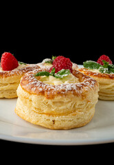 Close-up of raspberry puff pastry dessert with cream and mint on black background