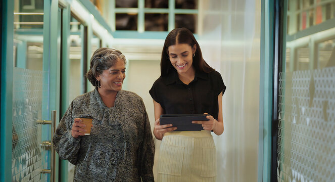 Indian older woman lady talk gossip young adult staff discuss work day time task indoor office place smiling female hold paper cup drink coffee expert girl hold tablet device walk at hall way space