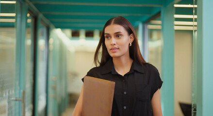 Indian happy young adult gen z woman lady hold file in hand walk indoor office hall way place...
