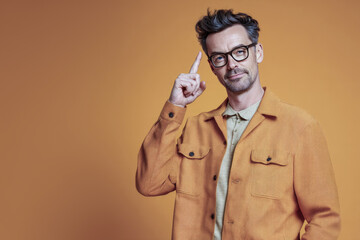 Creative man having an idea pointing at his temple wearing glasses and an orange jacket