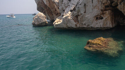 Yacht holidays in the Mediterranean Sea. In the sea, near the rocks, people relax on yachts. A sea boat is visible next to the rock. In summer, people relax on a yacht in the sea next to large rocks.