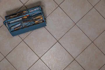 Open blue metal toolbox with visible old tools on tiled floor
