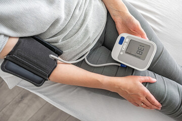 A person checks their blood pressure using a digital monitor while sitting indoors, highlighting a...